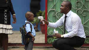 A school official shows a pupil an infrared digital laser thermometer before taking his temperature in Lagos, Nigeria, in September. Starting this week, similar hand-held devices are checking foreheads for fever at some U.S. airports.