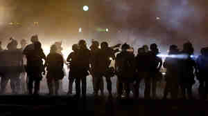 Police walk through a cloud of smoke as they clash with protesters in Ferguson, Mo., this summer.