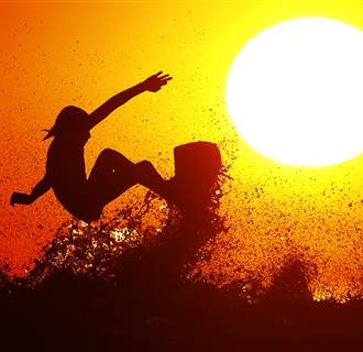 Surfer Cole Clisby rides his surfboard off the top of a wave as the sun sets off the shores of Leucadia