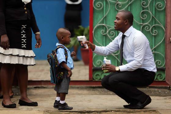 A school official takes a pupil's temperature using an infrared digital laser thermometer in front of the school premises, at the resumption of private schools, in Lagos