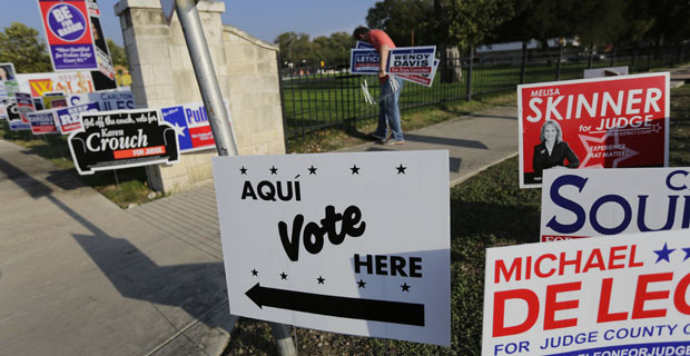 A campaign worker places campaign signs outside an early voting polling site, Monday, Oct. 20, 2014, in San Antonio. Early voting began Monday across Texas, where there are hotly-contested races for the state's high courts.