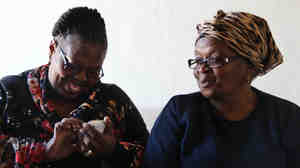 Gloria Gxebeka (left) visits Leona Mqhayi and types her health information into a cell phone