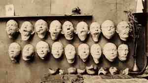 Plaster casts taken from soldiers' mutilated faces (top row), new sculpted faces (bottom row), and final masks (on the table) sit in the studio of Anna Coleman Ladd in 1918.