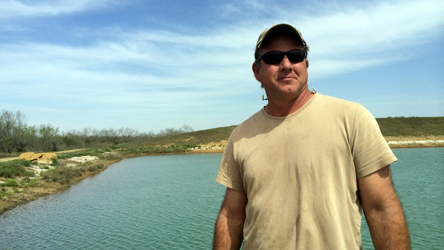 Rancher Darrell Brownlow stands in front of the pond Chesapeake Energy dug on his land when he leased part of it to the company. It will allow him to irrigate, and the oil money means he can afford to rebuild the ranch and bring back the cattle.