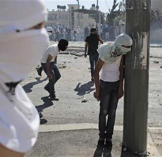Image: A Palestinian stone-thrower takes cover behind a street pole during clashes with Israeli police in Shuafat