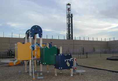 A Fort Worth, Texas, drill rig operated by XTO Corp. is located adjacent to the playground of a private day-care center. A sound wall separates the playground and the rig.
