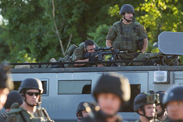  A police officer atop an armored vehicle looks through the scope of a rifle towards a crowd of demonstrators gathered to protest the fatal police shooting of Michael Brown in Ferguson, Mo., Aug. 12, 2014. The militarized police response to the protests over the shooting of an unarmed teenager has elicited a broad call from across the political spectrum for America’s police forces to be demilitarized. (Whitney Curtis/The New York Times