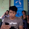 A man uses a mobile phone in front of a Telenor ad for cheap sim cards in Yangon, Myanmar. Cheap mobile technology has ignited an Internet revolution in the once-isolated nation.