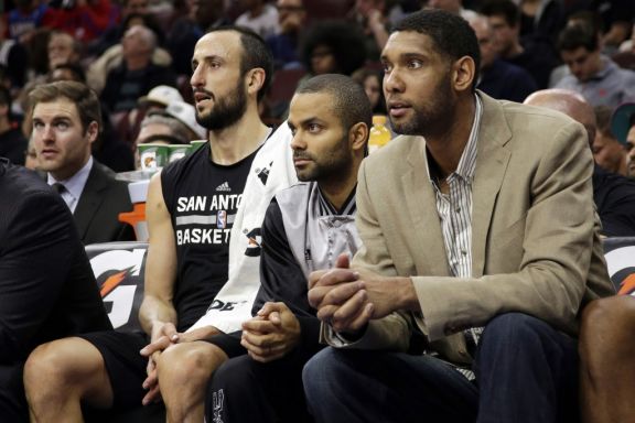 San Antonio Spurs' Tim Duncan, from right, Tony Parker, of France, and Manu Ginobili, of Argentina, watch from the bench during the first half of an NBA basketball game against the Philadelphia 76ers, Monday, Dec. 1, 2014, in Philadelphia. (AP Photo/Matt Slocum)