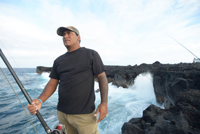 Desmond Valentin checks out his fishing gear as waves crash against the Hawaiian coast. Mr. Valentin once caught a 136.6-pound ulua.