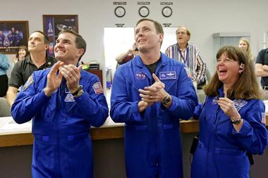 NASA astronauts, from left, Rex Walheim, Jack Fischer and Cady Coleman, cheer as they watch the landing of the Orion test flight on a television at the Press Site at the Kennedy Space Center, Friday, Dec. 5, 2014, in Cape Canaveral, Fla. The unmanned test flight ended 4ý hours after it began. (AP Photo/John Raoux)