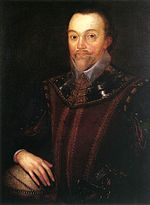 Man with high forehead and short pointed beard, in dark clothing which incorporates a shining leather or metallic collar. His right hand is resting on a globe of the world.