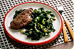 A plate with steak and spinach on it.