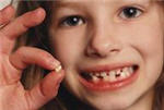 Young girl smiling and holding tooth.