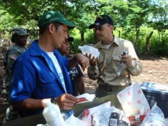 LCDR Gregory Langham, veterinarian, U.S. Public Health Services (right) and a veterinarian from the Nicaraguan Ministry of Agriculture and Forestry (left) teach a third-year Nicaraguan veterinary student aspects of parasitology and pharmacology. SGT Leona Thomas (in the background) observes. 