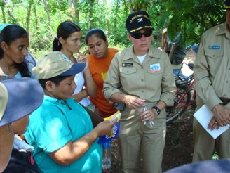 Under shade trees near a clinic in Acajutla, El Salvador, CAPT Cynthia Kunkel provides food-service training to volunteers who work on environmental health issues (latrines, food safety, water quality, etc.) in the surrounding communities. She also provided stem thermometers; the naval officer to her left served as interpreter.  