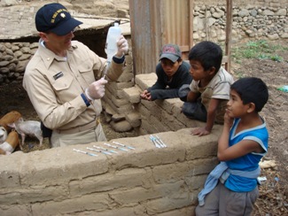 LCDR Gregory Langham, HHS Commissioned Corps veterinarian, in the midst of de-worming eight piglets; three young Peruvian boys observe on the right.