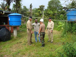  La Sierpe, Colombia.  (Left to right) CAPT Phil Rapp, Engineer, U.S. Public Health Service (USPHS); a community leader; an interpreter; and CAPT Craig Shepherd, Environmental Health Officer, USPHS discuss, at the rear of the La Sierpe’s elementary school, the school’s water supply catchment and containment system. 