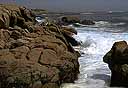 Large brown rocks protruding into surf along shoreline