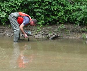 USGS scientist measuring pH and other water properties on the banks of Fourmile Creek, Iowa, before collecting a sediment sample for laboratory biodegradation experiments
