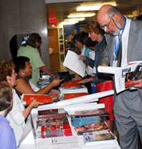 Teachers browse reading material spread on tables, and chat with Dept. employees seated behind tables answering questions and handing out brochures.