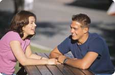 photo of teenage boy and girl seated at table talking to each other
