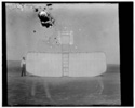  Orville at left wing end of upended glider, bottom view; KittyHawk, North Carolina 