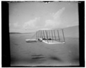  Wilbur Wright in prone position on glider just after landing, its skid marks visible behind it and, in the foreground, skid marks from a previous landing; Kitty Hawk, North Carolina
