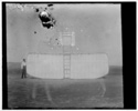  Orville at left wing end of upended glider, bottom view; KittyHawk, North Carolina 