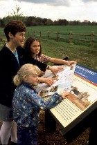 A family learns from the information at a Virginia Trails wayside marker.