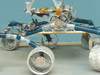 In this image, a large, six-wheeled rover sits on a concrete floor in a laboratory against a light-blue background.