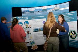 Casey Ralston (right) uses a popular interactive display to show how humans and oceans are connected and describe the research conducted by the West Coast Center for Ocean and Human Health.