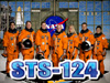 Seven astronauts in orange launch and entry suits stand behind the words STS-124
