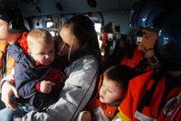 A mother holds her children in the safe confines of a Coast Guard helicopter as Petty Officer 2nd Class Travis Vanzandt looks on during the Northwest flood incident in Washington