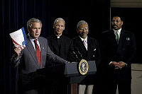 Holding up a book about his Faith-Based Initiatives, President George W. Bush talks with urban leaders in the Eisenhower Executive Office Building Wednesday, July 16, 2003.  Standing behind the President are, from left, Rev. Bishop John Juston Ricard of Fla., Rev. Eugene F. Rivers III of Mass., and Tony Evans of Texas.