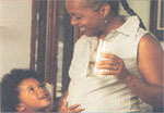 A pregnant woman drinking a glass of water and her child touching her stomach.