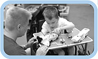 A man helping a child in a wheelchair with a toy.
