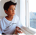 A young boy sad, looking out a window