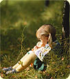 A little girl sitting alone in a green field.