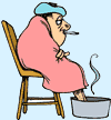 Image of man sitting in a chair with a blanket, thermometer, his feet in hot water, and a compress on his head