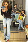 A woman bowling with a woman and man watching.