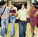 Three female students and one male student, talking, walking down a school hallway.
