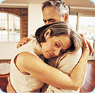 A man and woman hugging; both looking worried.