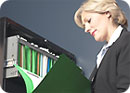 A woman standing by a file cabinet looking at a file folder.