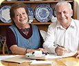 An older man and older woman smiling, doing paperwork with a calculator.