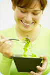 A woman eating a bowl of salad.