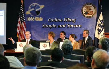 Photo showing (Back row) USPTO Director Jon Dudas and Secretary of Commerce Carlos Gutierrez looking on as (front row) Dean Harts of 3M, April Sauders-Fuller of Fish & Richardson, and Felicia Metz of the University of Maryland file patent documents electronically at the March 16, 2006 launch of the USPTO's new Electronic Filing System-Web (EFS-Web).