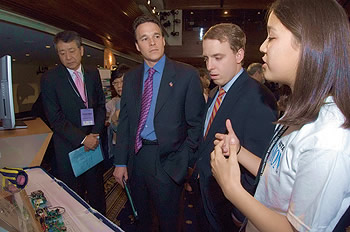 Photo showing Chairman and CEO of Toshiba America Toru Uchiike (left) and USPTO Director Jon Dudas (center left) observing a demonstration from Amy Hafer of her team's winning invention, 'The Human Touch.'   The event was the ExploraVision Awards Program, one of the world's largest science and technology competitions for students (K-12th grade).  It is sponsored by Toshiba America and administered by the National Science Teachers Association.