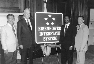 The standard road sign for the Dwight D. Eisenhower National System of Interstate and Defense Highways, designed by FHWA and the American Association of State Highway and Transportation Officials, was unveiled in a ceremony on Capitol Hill on July 29, 1993. Left to right: Chairman Nick J. Rahall (D-WV) of the House Surface Transportation Subcommittee, John Eisenhower  (President Eisenhower's son), Federal Highway Administrator Rodney E. Slater, and Chairman Norman Y. Mineta (D-CA) of the House Committee on Public Works and Transportation.