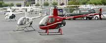 photo: two white helicopters on tarmac and a red one a few feet above ground